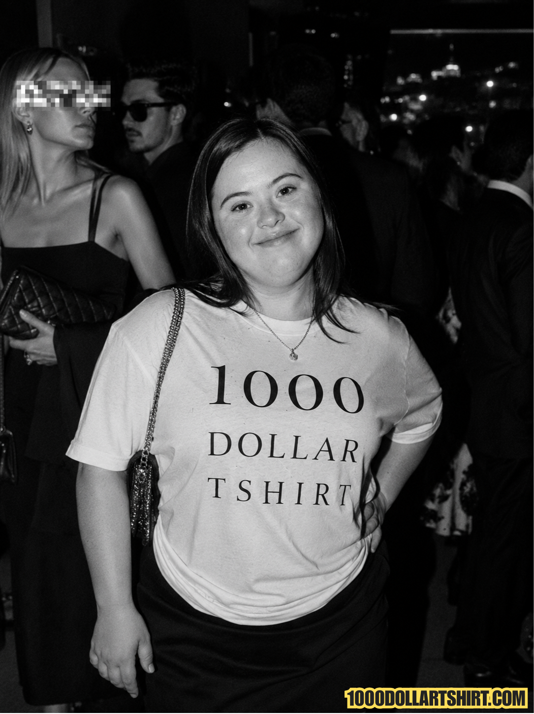 Black and white portrait of a smiling young woman with Down syndrome wearing a 1000 Dollar T Shirt at an elegant evening event surrounded by formally dressed guests.