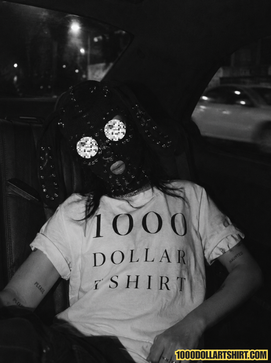Black and white candid photograph of a woman wearing a studded bunny balaclava and a 1000 Dollar T Shirt while sitting in the back seat of a car at night.